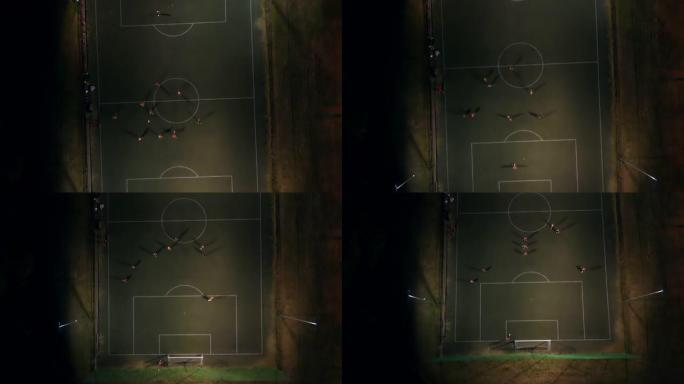 鸟瞰图。小男孩在夜间体育场鸟瞰图与教练踢足球。无人机在足球场射击，青少年在夜间体育场踢足球。