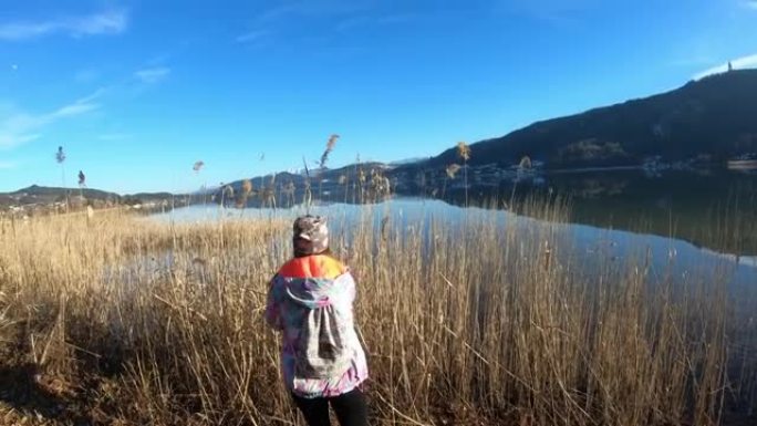 一个穿着花帽的女人沿着奥地利沃瑟湖 (Woerthersee Lake) 长满的甜美旗帜海岸漫步，享