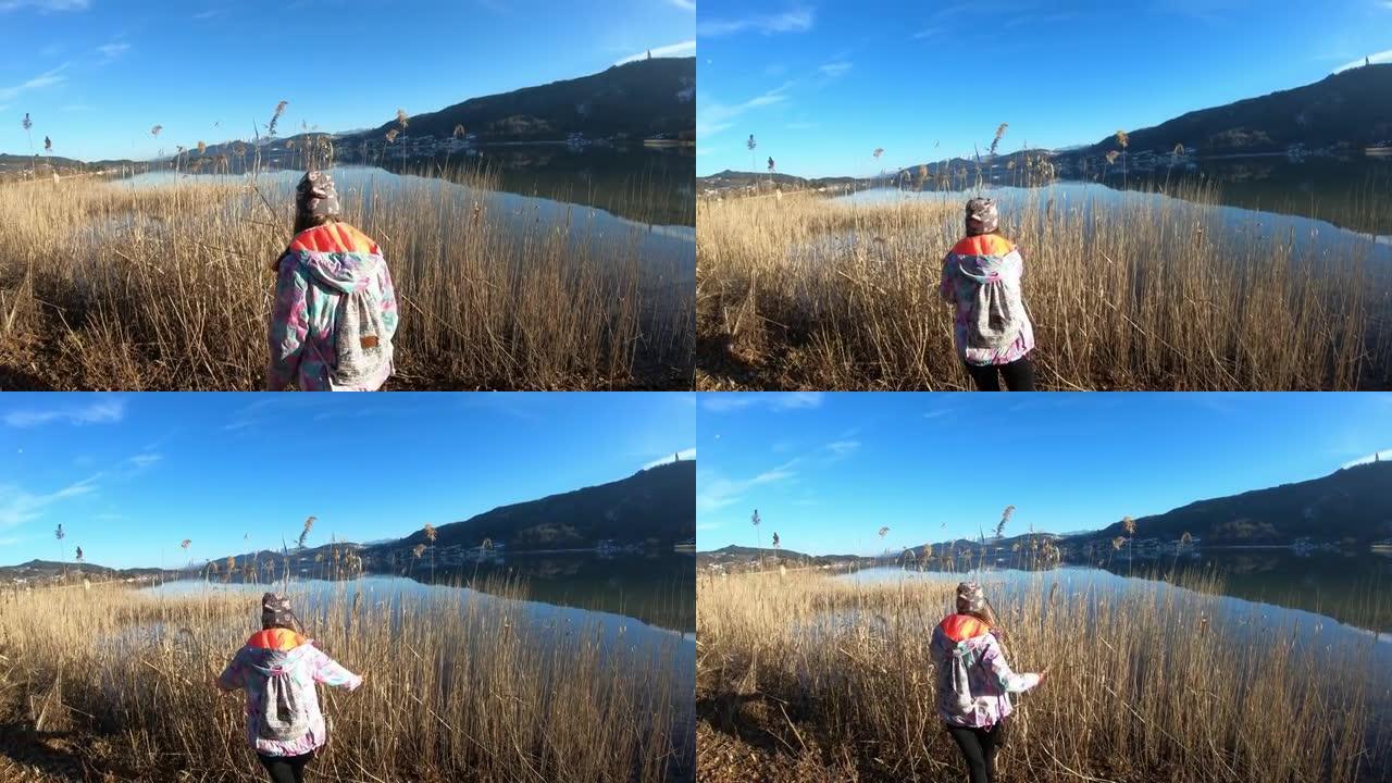一个穿着花帽的女人沿着奥地利沃瑟湖 (Woerthersee Lake) 长满的甜美旗帜海岸漫步，享