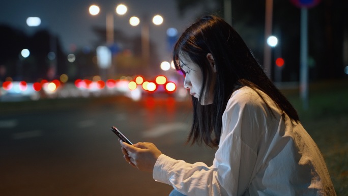 夜晚女孩在街边玩手机