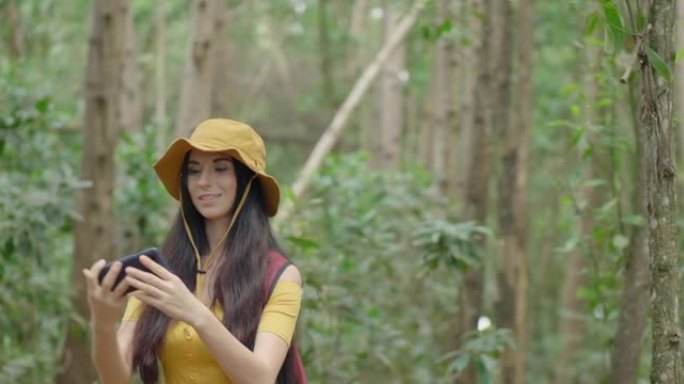 假期在树林里散步的年轻女子感到高兴和精神焕发。举起手机，用大自然给自己拍照