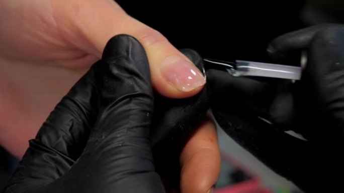 经验丰富的美甲师在拇指指甲上使用基础凝胶