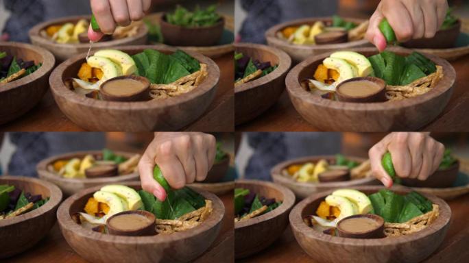 用手将酸橙挤在健康的绿色沙拉上，豆腐和鳄梨。为朋友准备晚餐