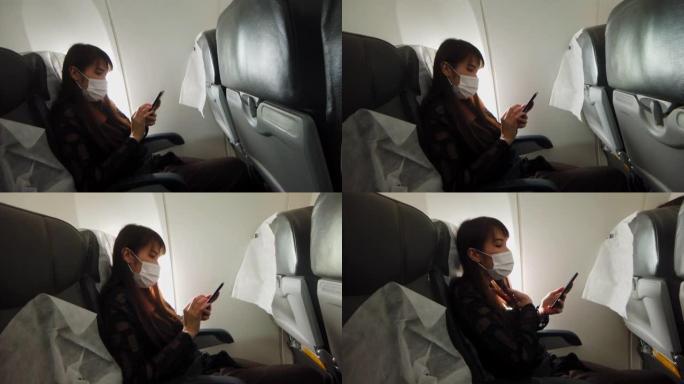 戴口罩的亚洲女性在飞机座椅上使用手机