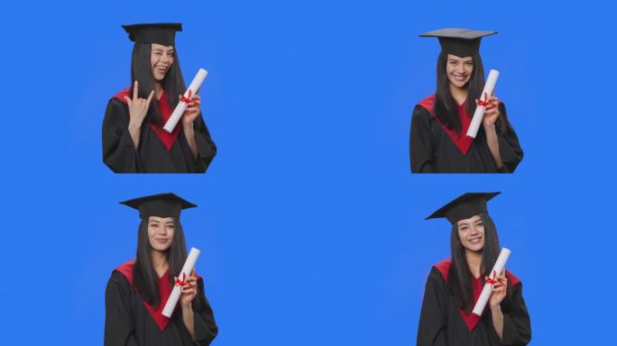 穿着便帽和长袍毕业服装的女学生肖像，拿着文凭和做摇滚手势。年轻女子在工作室摆姿势，蓝屏背景。特写。慢