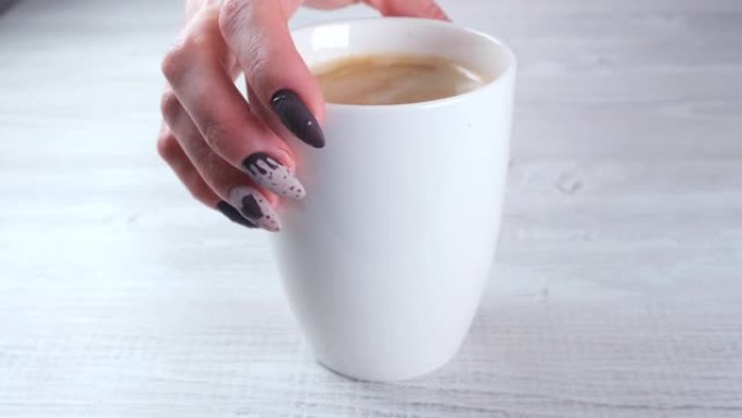 美丽的修剪过的指甲，以巧克力糖的形式出现在女性的双手特写和一杯咖啡上