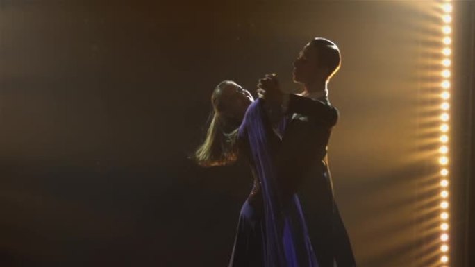 由专业舞厅舞者表演的古典华尔兹。剪影年轻男女练习舞步，在黑暗的工作室里用烟雾和聚光灯在地板上表演。特