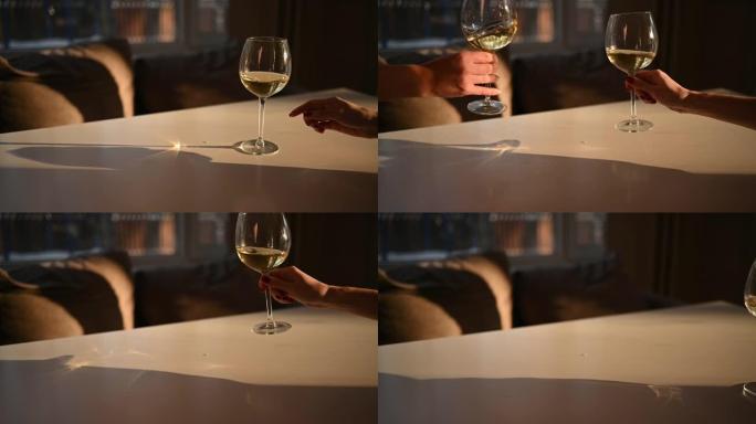 女性的手在白色桌子上碰杯，配以干白葡萄酒。散焦模糊背景。用阳光关闭高脚杯内葡萄酒混合过程的慢动作视频