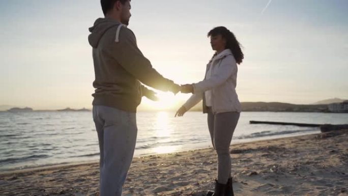 年轻的多种族非洲裔美国情侣在婚礼旅行中的浪漫场景日落时牵手在海滩上走向大海，在背光下与太阳接吻