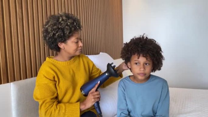 非裔美国母亲在卧室用吹风机吹干儿子的头发
