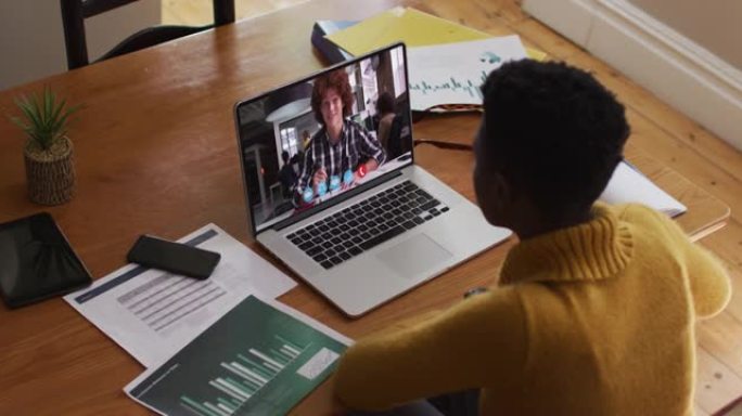 非裔美国女教师在家里用笔记本电脑进行视频通话时说话和做笔记