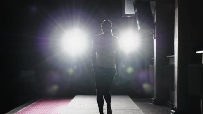 女子体操运动员在跳跃前直线奔跑，获得动力。在一个明亮的聚光灯下，在黑暗的健身房里进行跳跃推动向前翻转