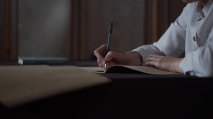 女性手工做笔记的特写视图，在老式素描本笔记本日记中写信。教育概念女人坐在办公桌前学习。书放在桌子上。