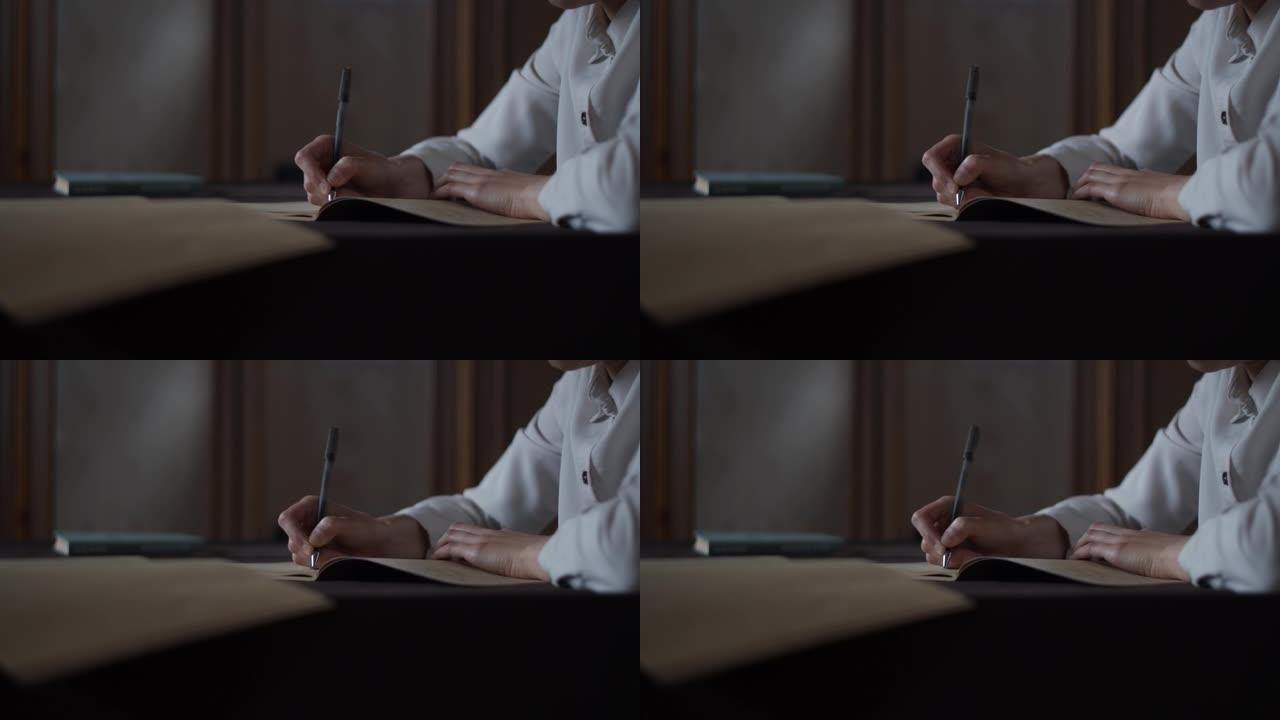 女性手工做笔记的特写视图，在老式素描本笔记本日记中写信。教育概念女人坐在办公桌前学习。书放在桌子上。