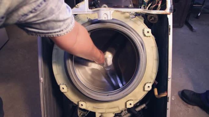 一个人的手转动洗衣机的滚筒和洗衣机。
