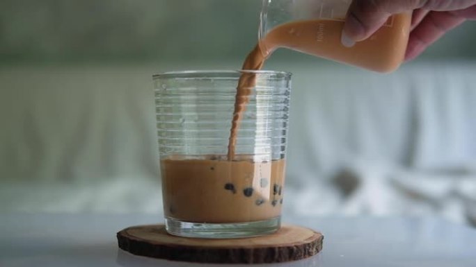 将泰国奶茶倒入装有木薯珍珠泡的玻璃杯中。慢动作