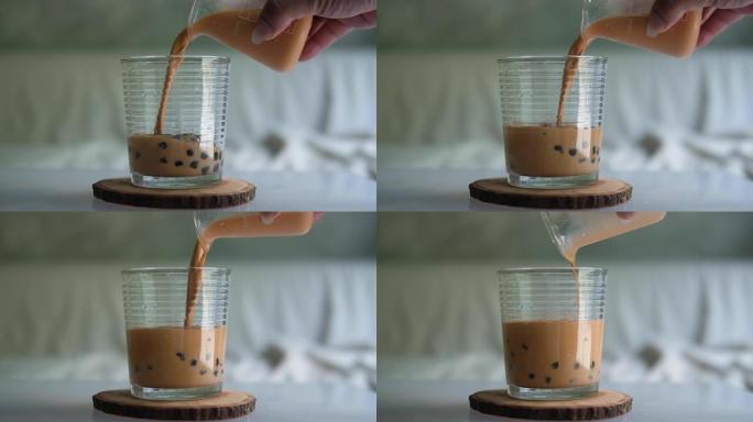 将泰国奶茶倒入装有木薯珍珠泡的玻璃杯中。慢动作
