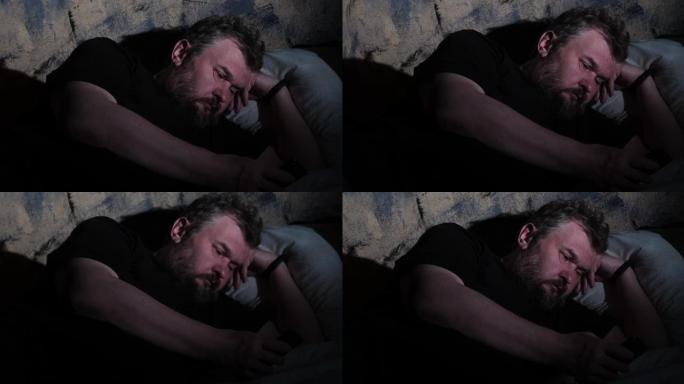 疲惫和情绪倦怠成熟的男人正躺在黑暗房间的床上，用他的智能手机