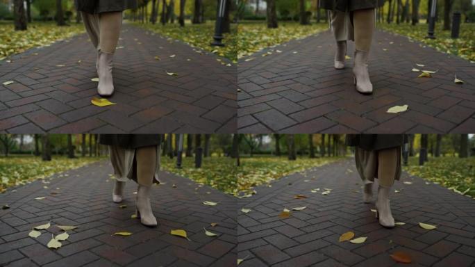穿着时尚靴子的女性脚在10月公园。女人的腿走的路。