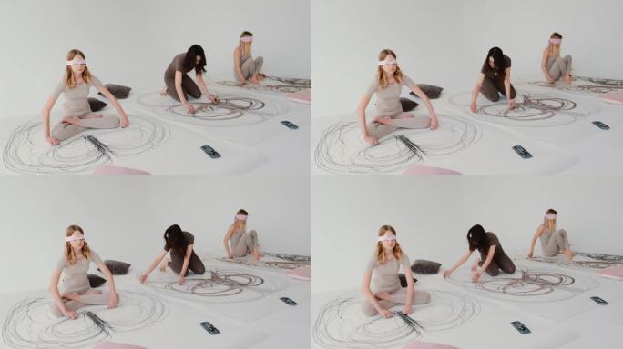 女孩在瑜伽中用粉彩画一幅抽象的图画，用手画画。轻盈通风的创意工作室，地板上有大画布。