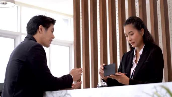 亚洲礼宾女在大堂柜台与商人交谈，以办理机场或酒店入住手续。员工接待员在旅行度假或商务旅行中预订付款。