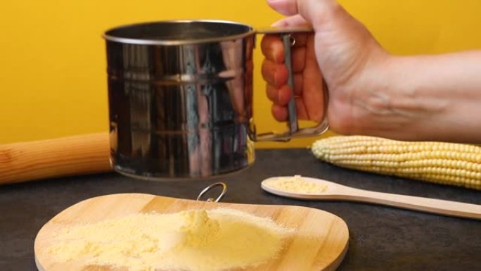 玉米生产产品的概念。厨师的手在木板上筛玉米粉，在黄色背景上筛新鲜玉米。