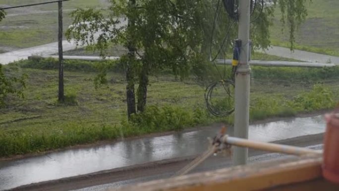 外面下着大雨。从窗户可以看到树木，道路和杆子。通常的城市景观