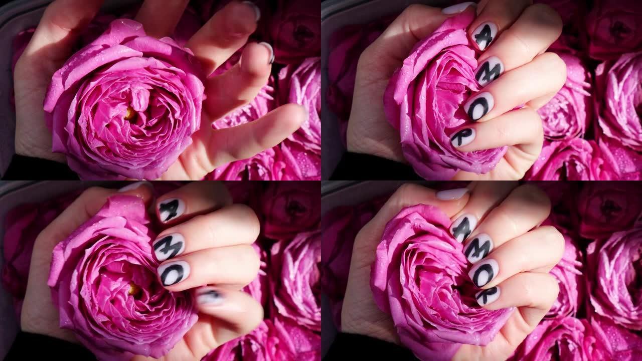 指甲修指甲上的一个字在黑色丝绸织物上保持粉红色的玫瑰花。最小的平铺性质。女性手。爱