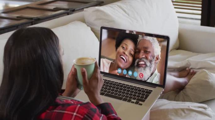 非裔美国妇女拿着咖啡杯，坐在家里沙发上的笔记本电脑上进行视频通话