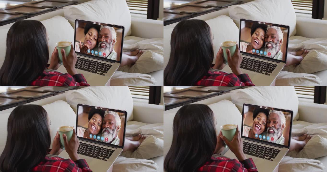 非裔美国妇女拿着咖啡杯，坐在家里沙发上的笔记本电脑上进行视频通话