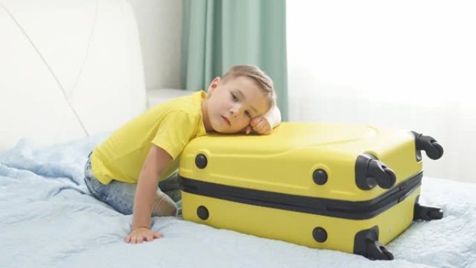 小男孩正坐在一个黄色的手提箱旁边等着度假。一个带行李箱的可爱孩子正在等待出租车去机场