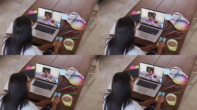 非裔美国女教师在笔记本电脑上与女孩进行视频通话时在备忘录笔记上写作