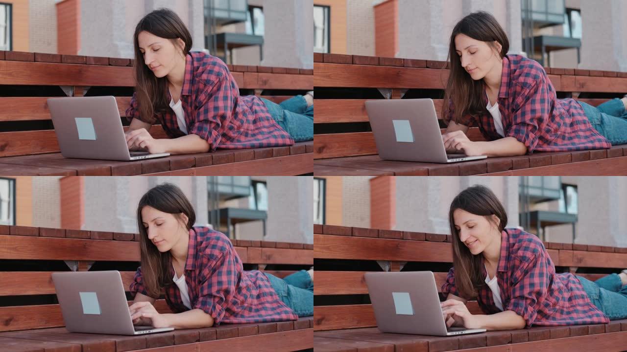在新鲜空气中在笔记本电脑上工作的女孩。满意的年轻女性自由博客作者在她的博客上发表文章