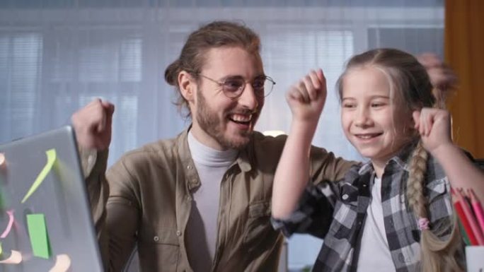 可爱的小女孩和开朗的父亲因冠状病毒而在远程教育期间在线上完成的课程中跳舞并欢欣鼓舞，看着相机