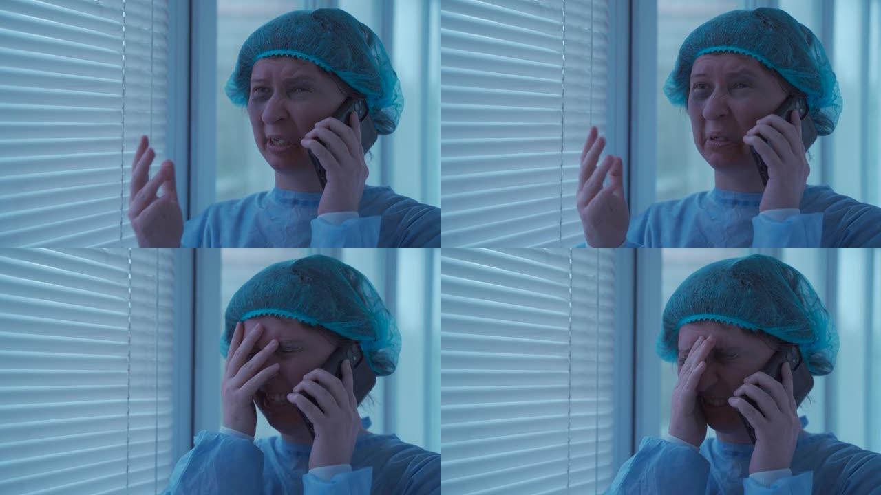 穿着一次性蓝色医用防护服和帽子的年轻女性患者不高兴，哭着打电话给急诊医院的保险公司，站在窗户旁边的走