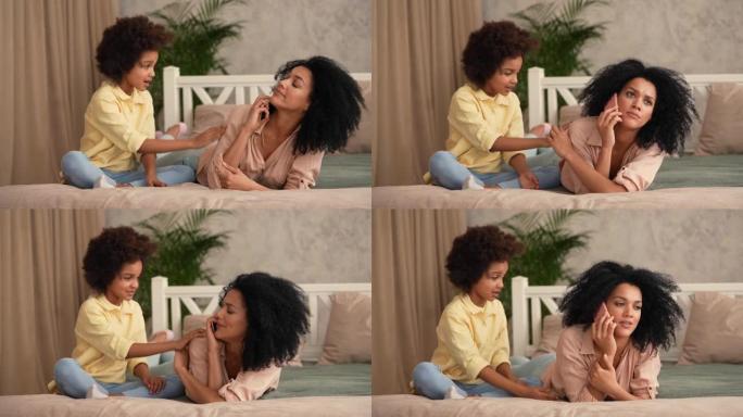 非裔美国妇女正在智能手机上聊天，而小女孩则分散了她的注意力。母亲和女儿躺在卧室的床上，室内明亮。慢动