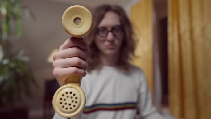 男性手中的黄色老式电话听筒的特写镜头，背景为模糊的20世纪80年代20世纪90年代书呆子。年轻的白人