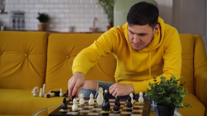 年轻人坐在黄色沙发上，在房间里下棋。男性与自己一起玩逻辑棋盘游戏