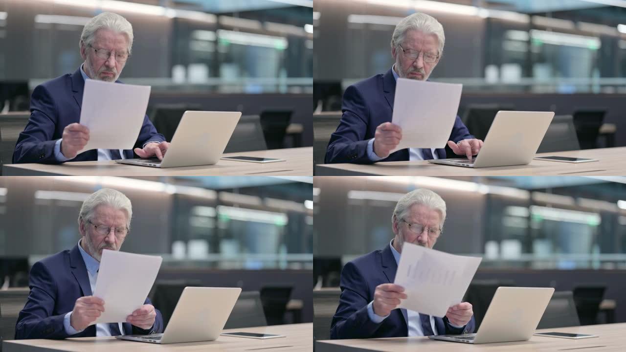 老商人阅读文件，在笔记本电脑上工作