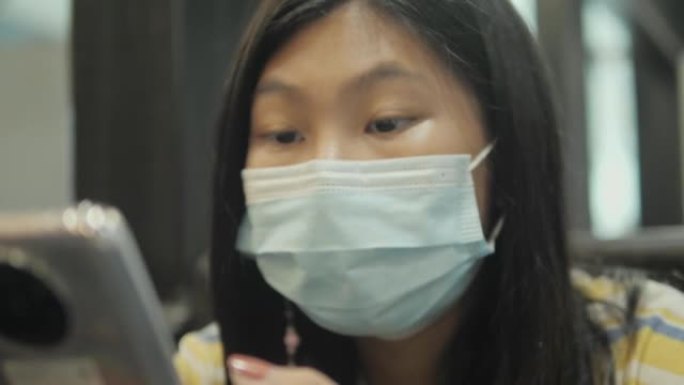 亚洲女孩戴着口罩使用智能手机等待她的食物在餐厅，生活方式的概念。