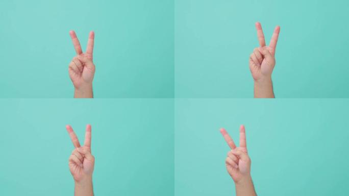 人手举的特写镜头，带有v形符号。表现出手势的人，其中食指和中指抬起并分开形成V。在背景的孤立蓝屏中看
