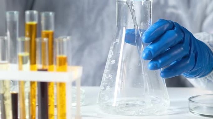 现代实验室的防护服和手套化学家将透明溶液倒入大型玻璃管中。实验室研究和制药技术。药理学工业中的生物学