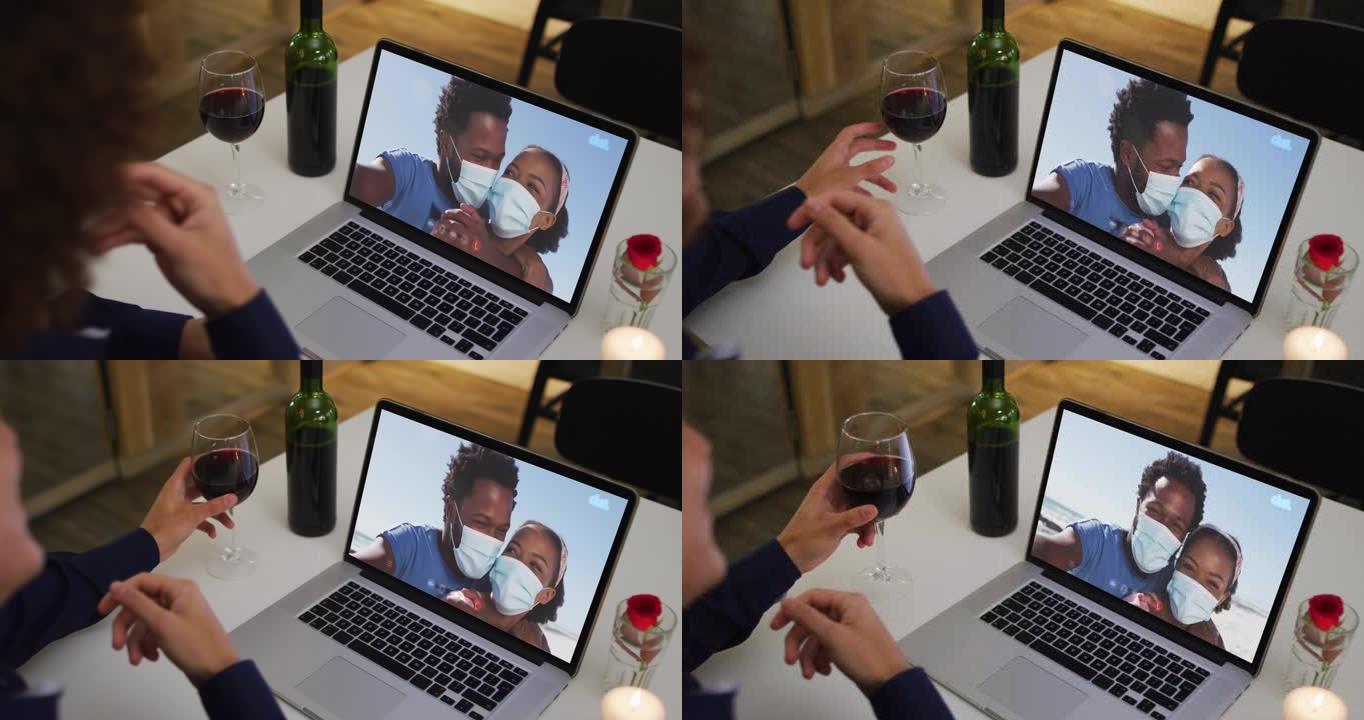 非洲裔美国妇女的中间部分拿着酒杯，同时在家里的笔记本电脑上进行视频通话