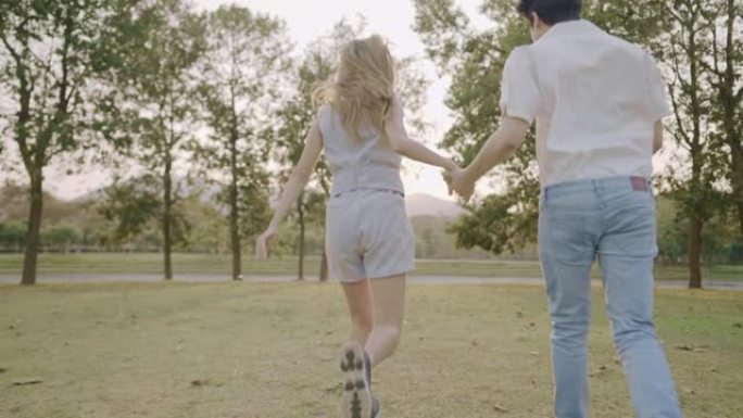 年轻的成年夫妇手牵着手穿过公园花园，走出城市，难忘的时刻