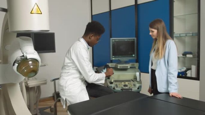 现代诊所的非裔美国家庭医生，拿着平板电脑向女性高加索患者展示肾脏和内脏的超声扫描并解释治疗方法