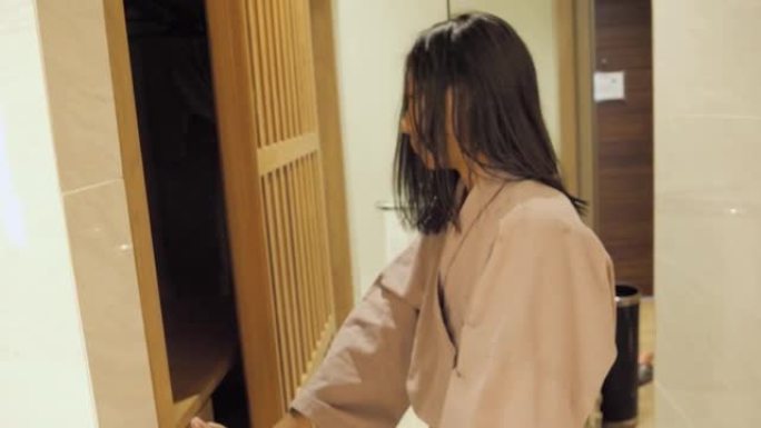 快乐的亚洲女孩穿着灰色浴袍，走出酒店的浴室，生活理念。