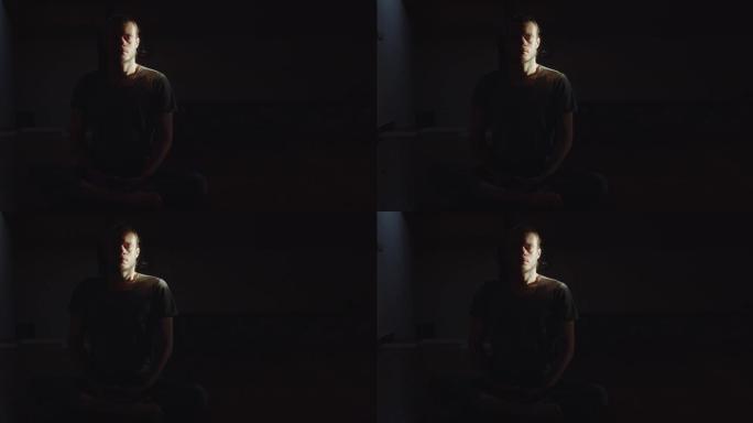 男人的肖像坐在莲花体式中独自冥想在黑暗的房间黑色背景复制空间。沉思平静瑜伽练习瑜伽冥想室内晨光文字。