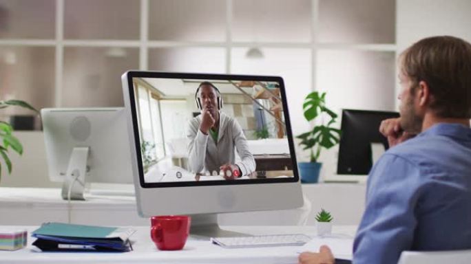 白人商人坐在办公桌前，使用计算机与男同事进行视频通话