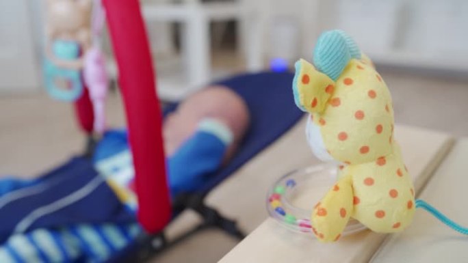 婴儿躺在婴儿摇椅上，为新生儿准备的色彩鲜艳的玩具拨浪鼓。