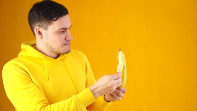 年轻人在黄色背景上剥香蕉的特写镜头。帅哥边看边剥水果